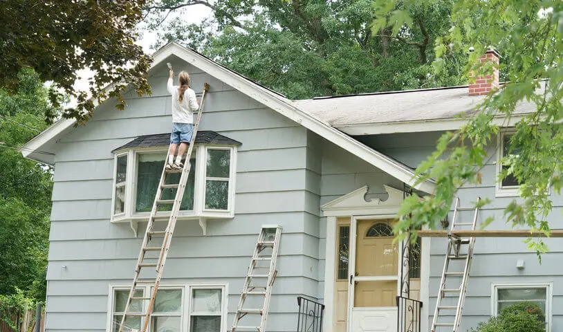 Home exterior being painted on a ladder during mild weather, illustrating the best time for exterior painting in Warwick NY