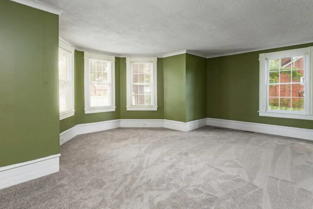 Empty living room with green walls and white trim, showing one of the factors that affect interior paint durability in an older home.