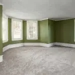 Empty living room with green walls and white trim, showing one of the factors that affect interior paint durability in an older home.