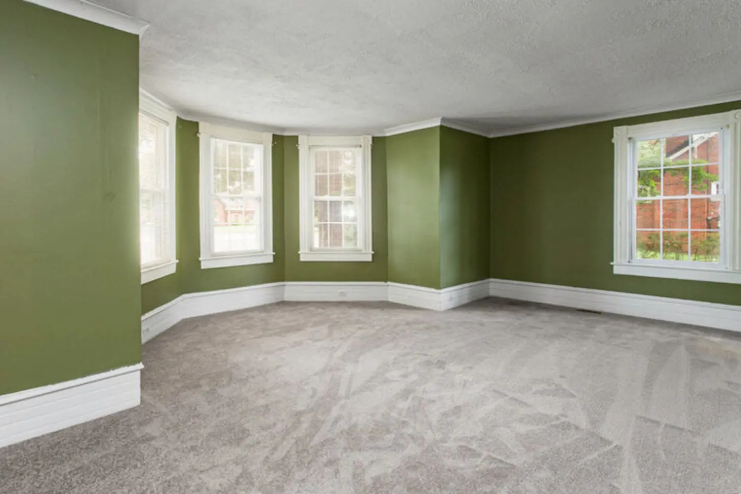Empty living room with green walls and white trim, showing one of the factors that affect interior paint durability in an older home.
