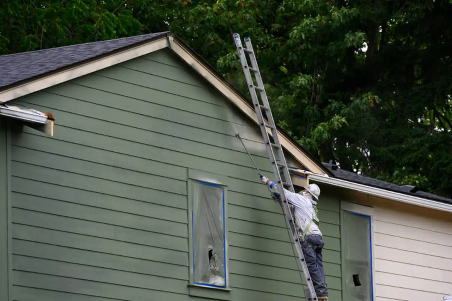 Professional painter on a ladder spraying exterior siding, illustrating how long professional exterior painting typically lasts.