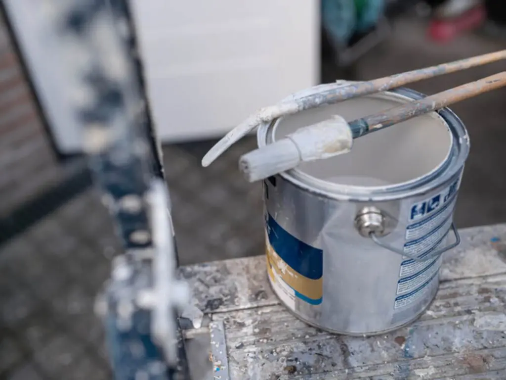 Paint can and brush on a ladder, representing the questions homeowners ask before hiring an exterior painting company.