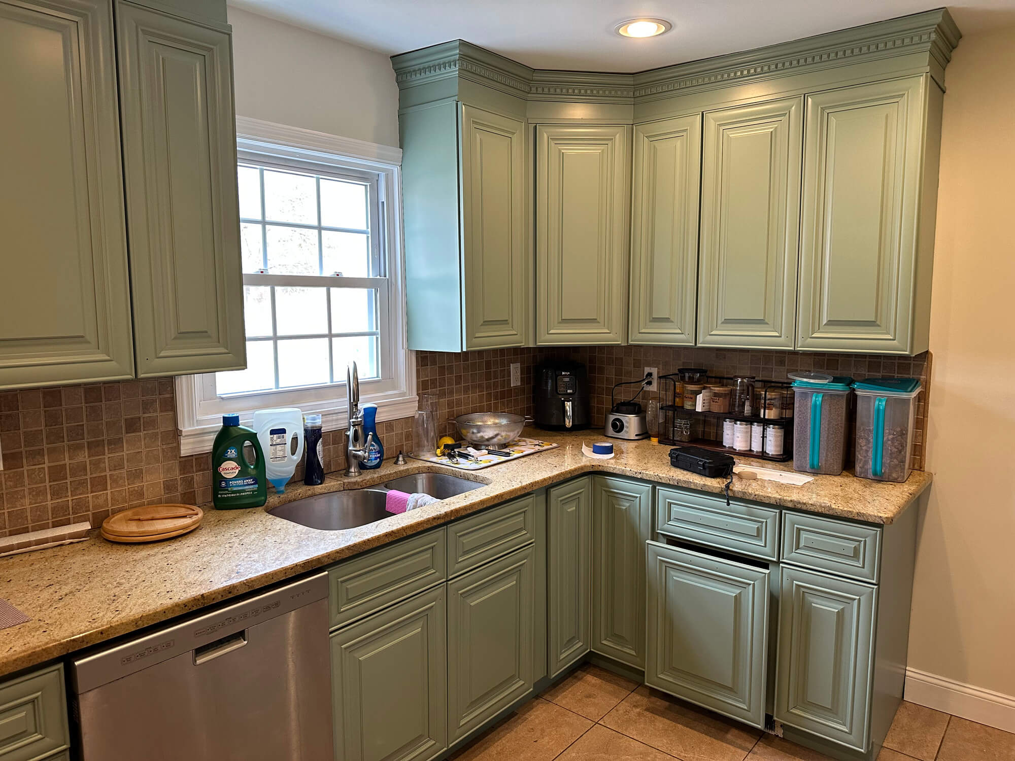 A kitchen featuring sage green cabinets, speckled beige granite countertops, stainless