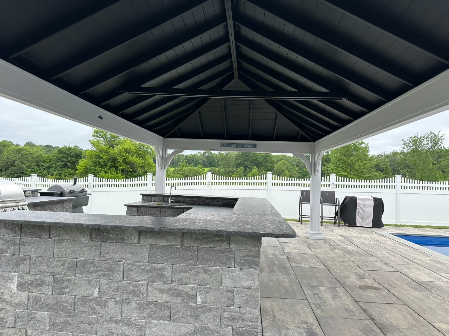 Deck Staining in Warwick, NY project featuring a beautifully painted black and white outdoor pavilion and custom stone kitchen by a pool.