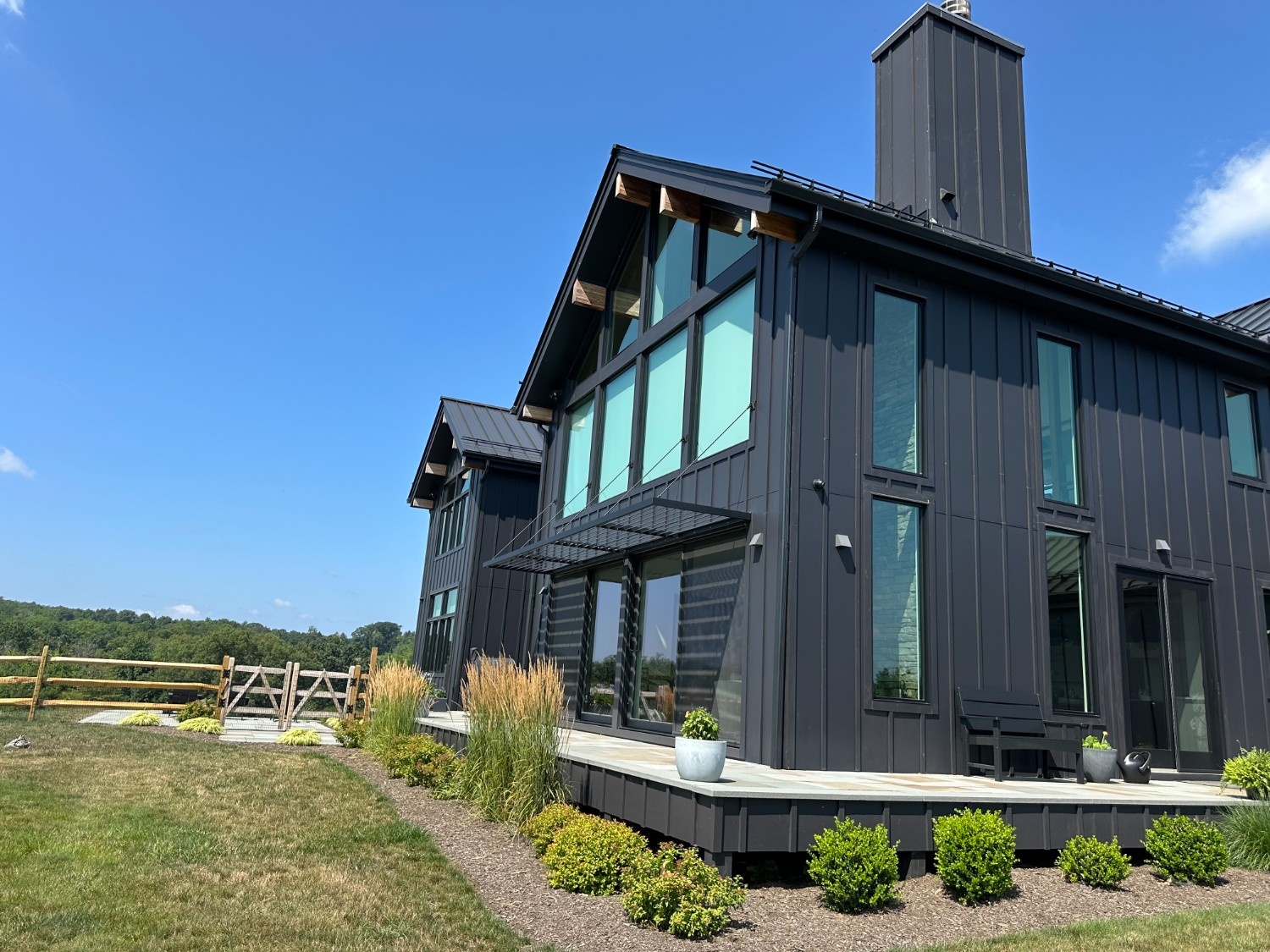 Professional Exterior Painting of a modern farmhouse featuring vertical black siding, large windows, and a wood deck.