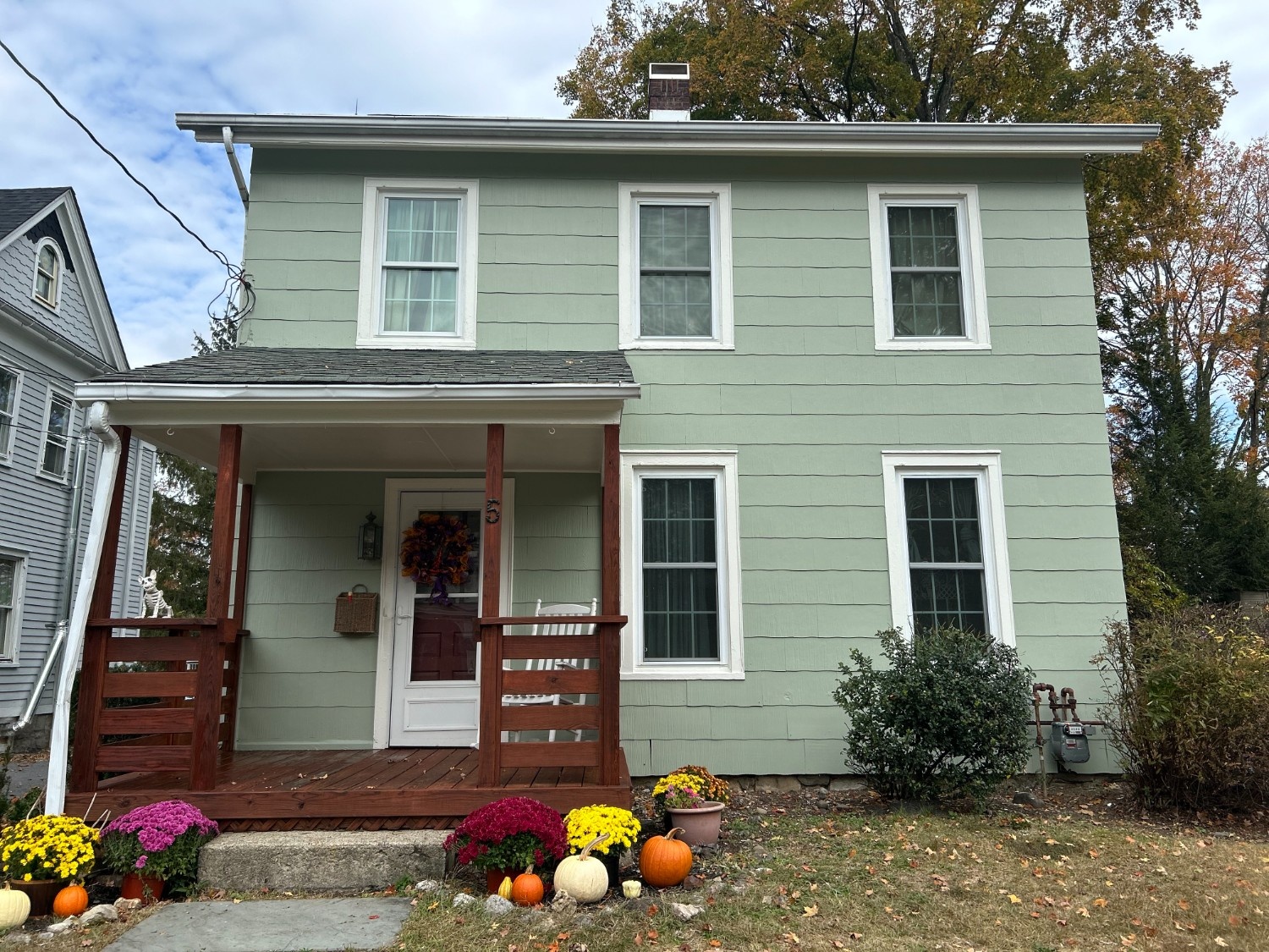 Professional Exterior Painting of a two-story home with soft sage green siding, crisp white trim, and a stained wood porch.