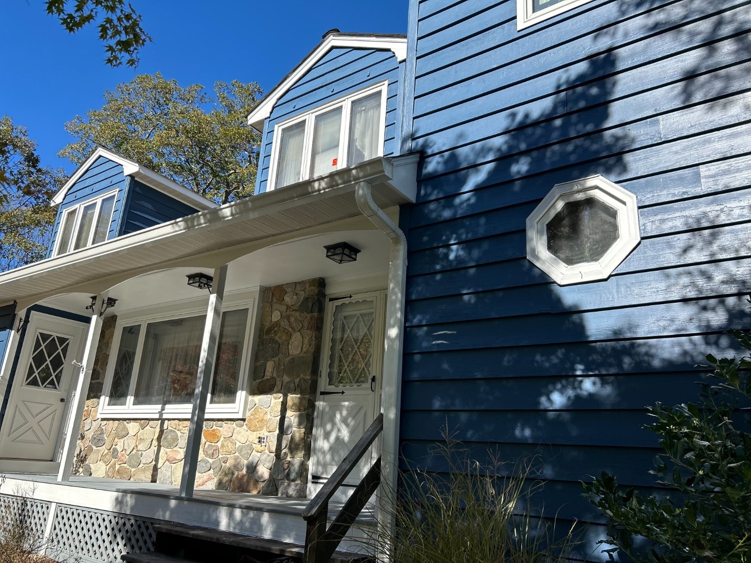Professional Exterior House Painting project showcasing deep blue clapboard siding, clean white trim, and a stone veneer porch entryway.