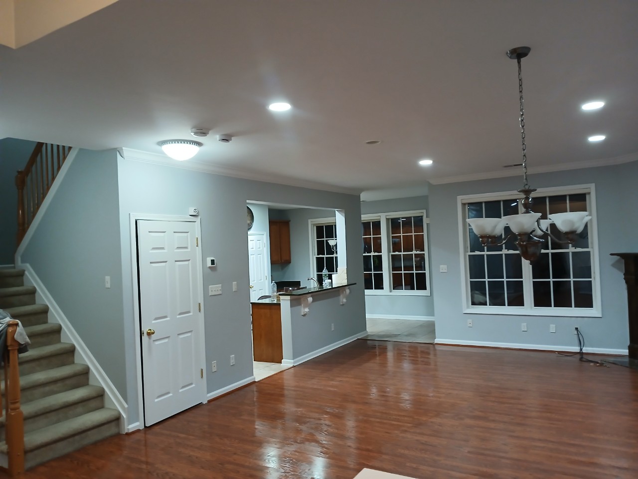 Home Improvement interior painting of a large, open-concept living area and staircase with light blue walls and glossy hardwood floors.