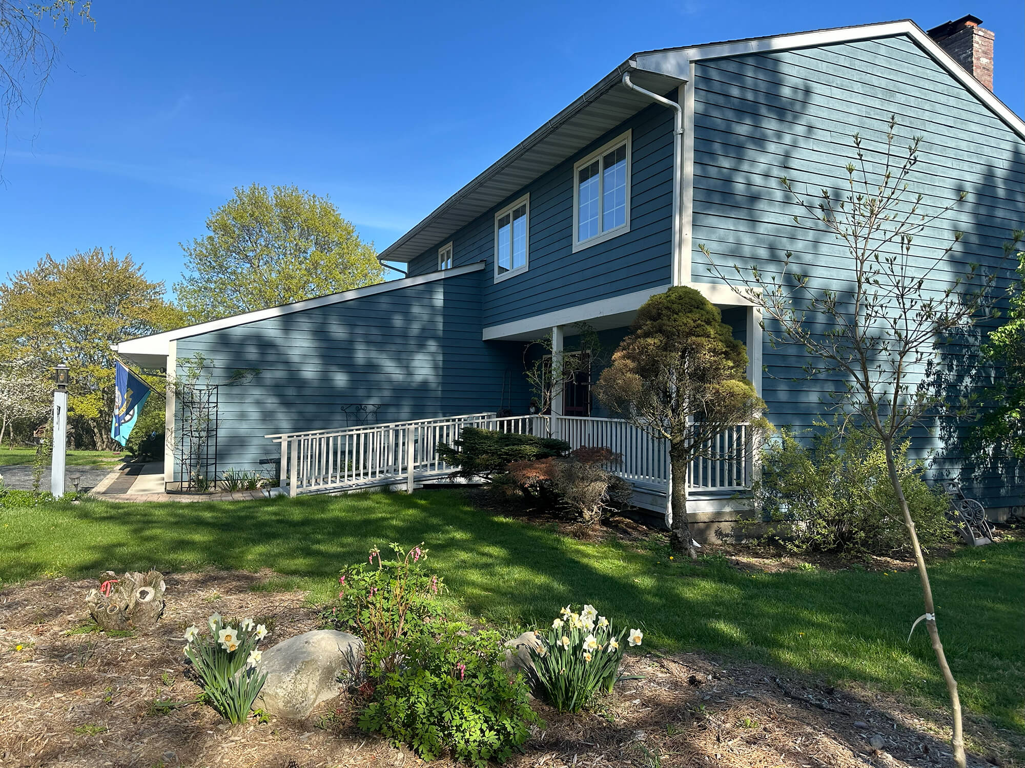 Residential home with recently painted blue-gray horizontal siding and white trim, featuring a front ramp and landscaped yard, showcasing the exterior work done by professional painters in Saddle River, NJ.