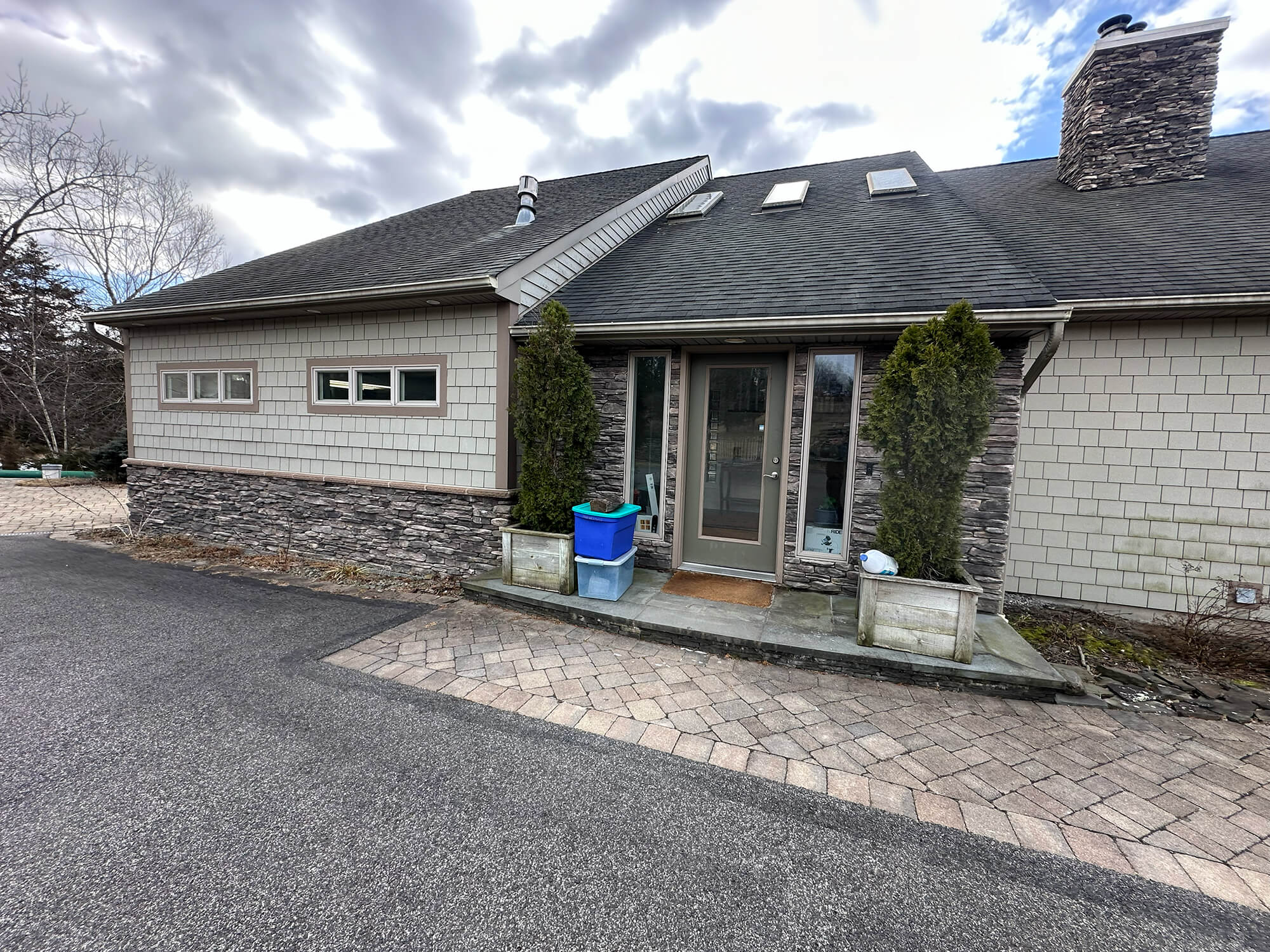 Exterior entrance of a residential home featuring light-colored shake siding and a dark stacked stone base, showcasing the premium finishes provided by skilled painters in Tuxedo Park, NY.