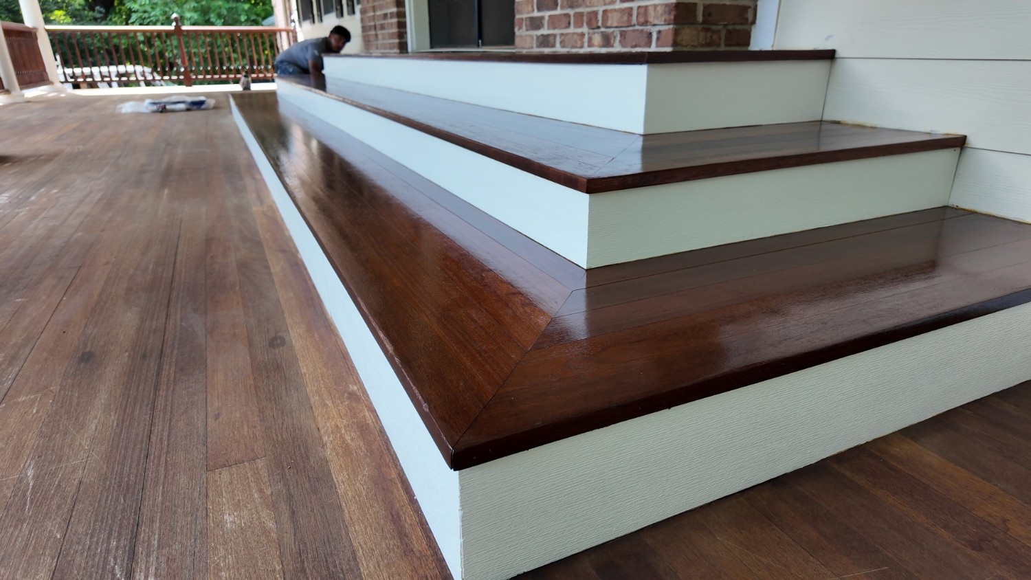 Professional exterior wood finishing project showing glossy stained stair treads and crisp white painted risers and stringers.