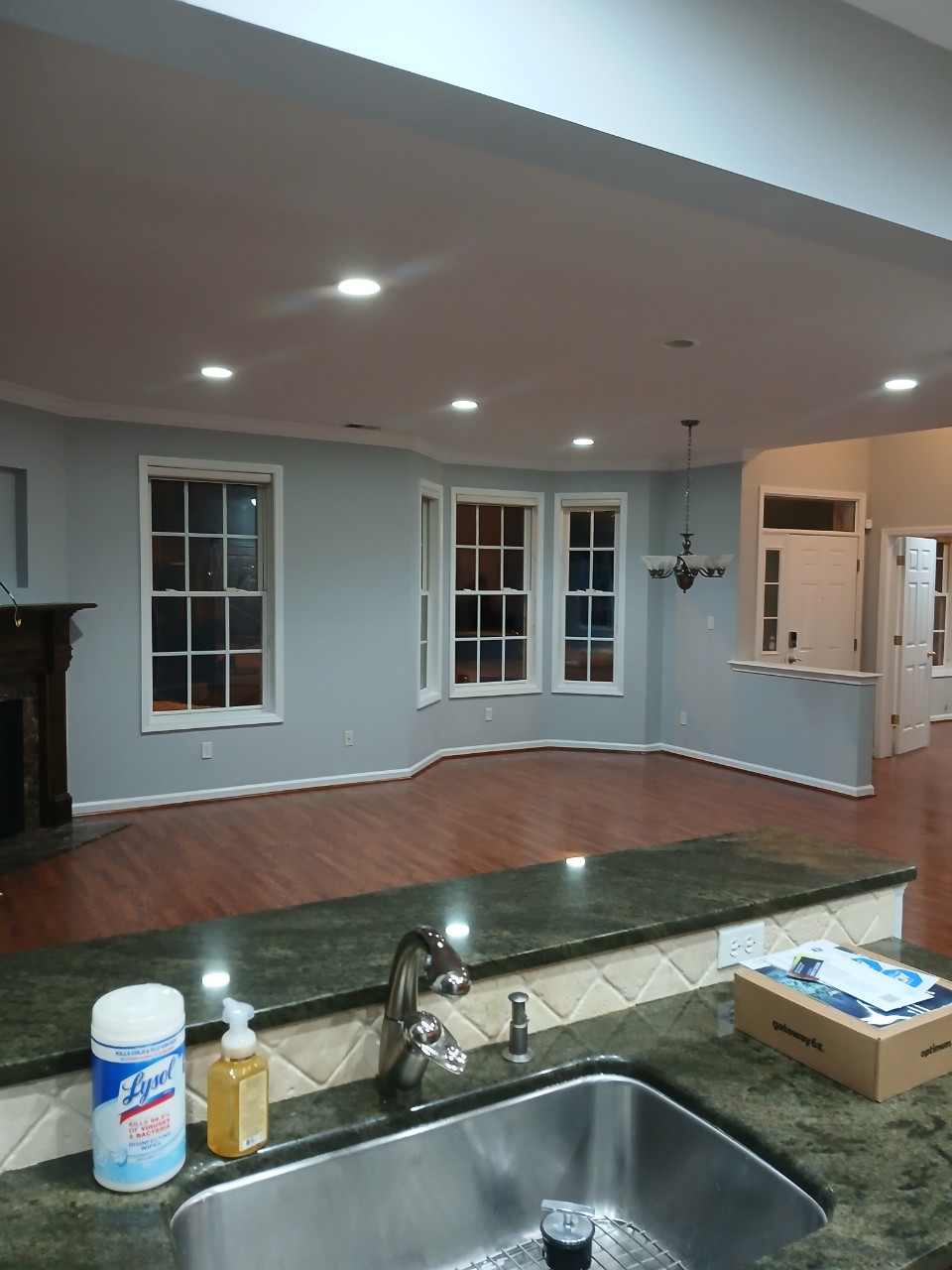 Interior painting of an open concept living area with light blue/grey walls, white trim, hardwood floors, and recessed lighting.