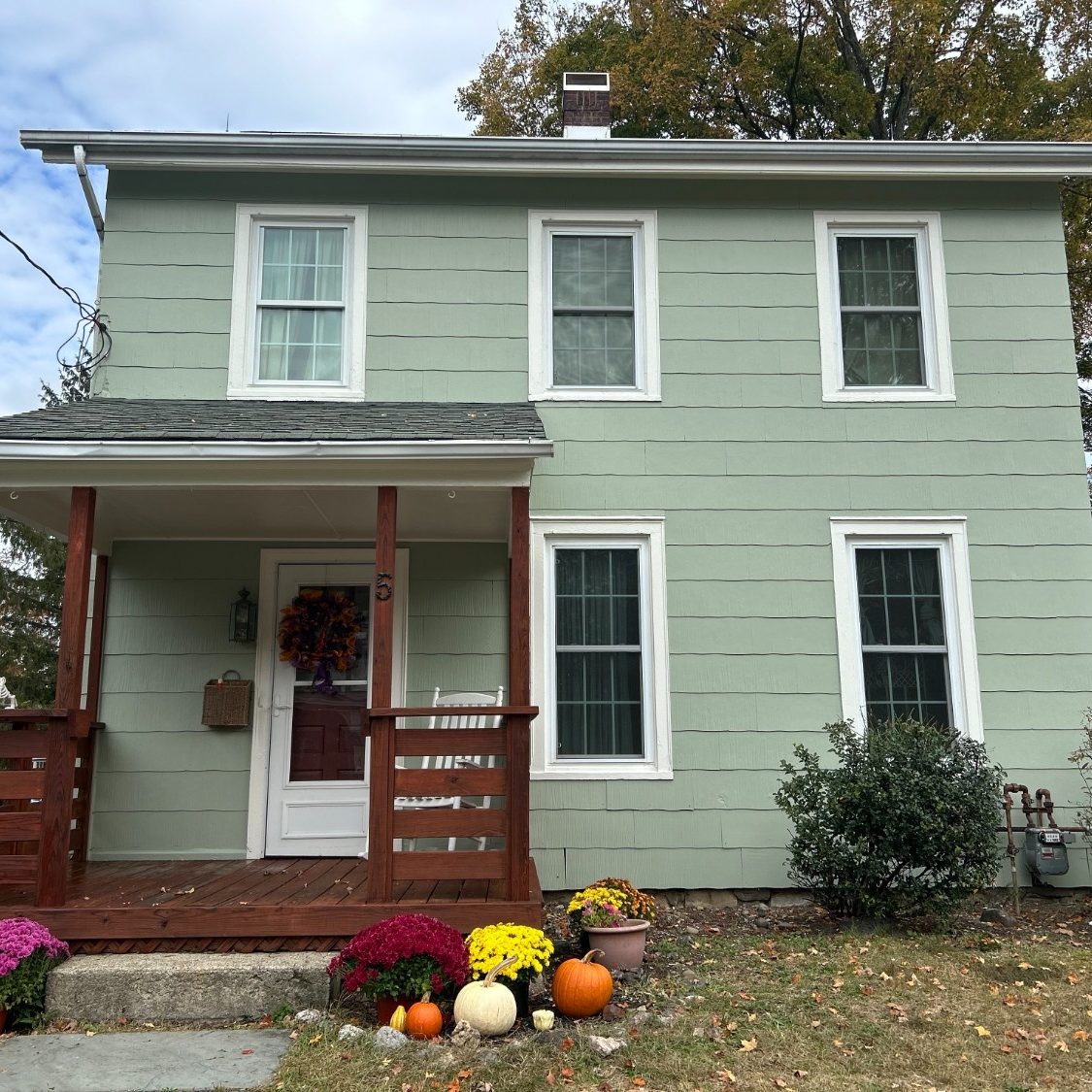 Professional Exterior Painting of a two-story home with soft sage green siding, crisp white trim, and a stained wood porch.