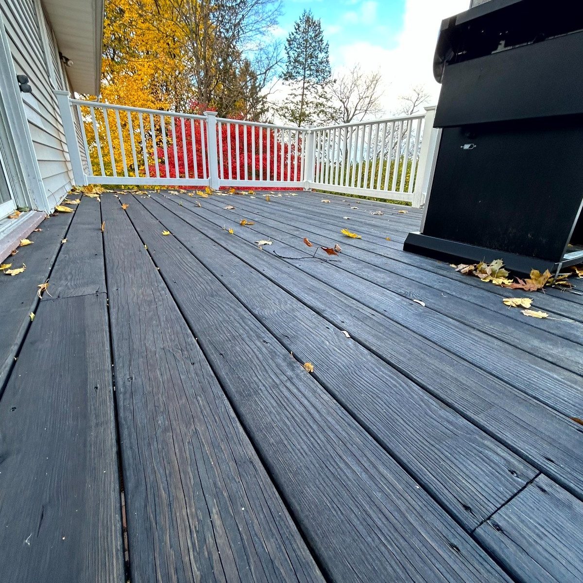 Professional Deck Staining service showing deep charcoal stain on wood planks and clean white painted deck railings.