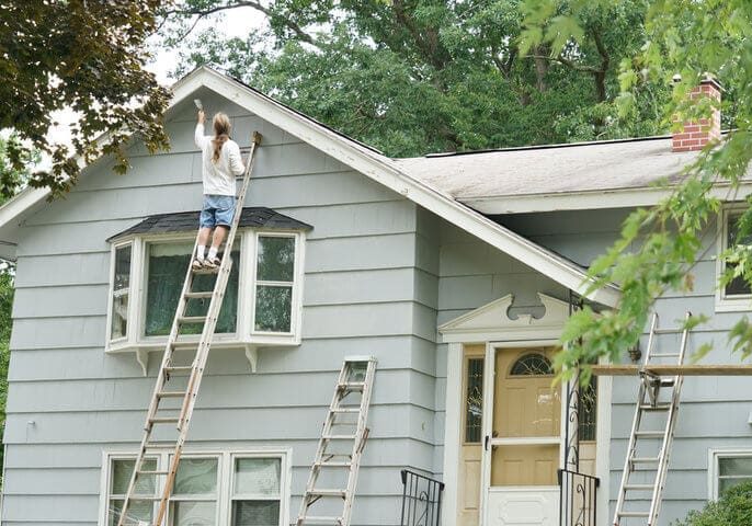 Home exterior being painted on a ladder during mild weather, illustrating the best time for exterior painting in Warwick NY
