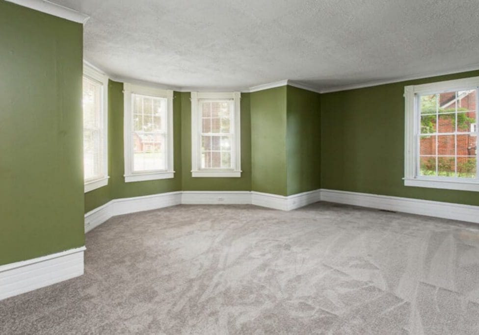 Empty living room with green walls and white trim, showing one of the factors that affect interior paint durability in an older home.