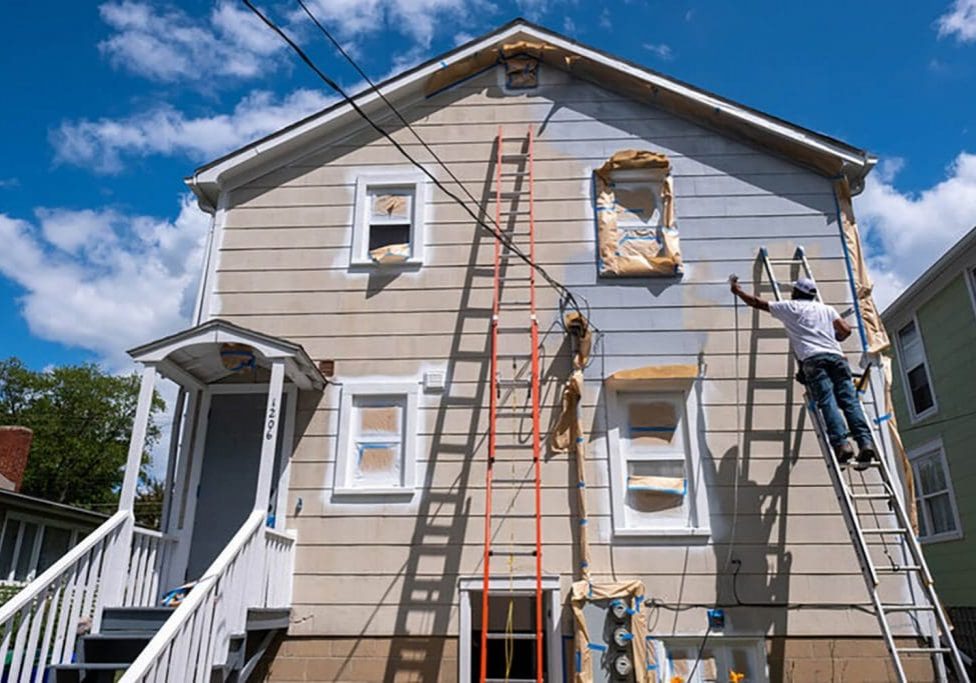 Professional painter applying fresh exterior coating on a two-story home, showing how weather affects exterior paint longevity in seasonal climates