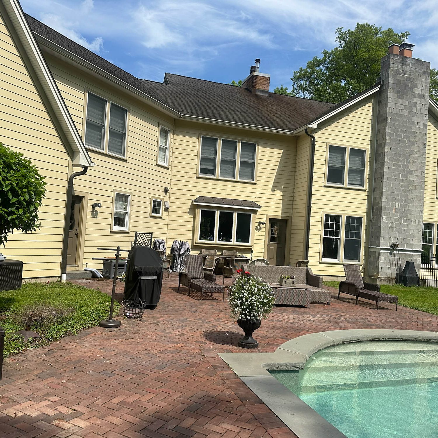 Large two-story home exterior painting by Willow Tree Painting & Home Improvement, featuring light yellow siding, a brick patio, and a swimming pool edge.